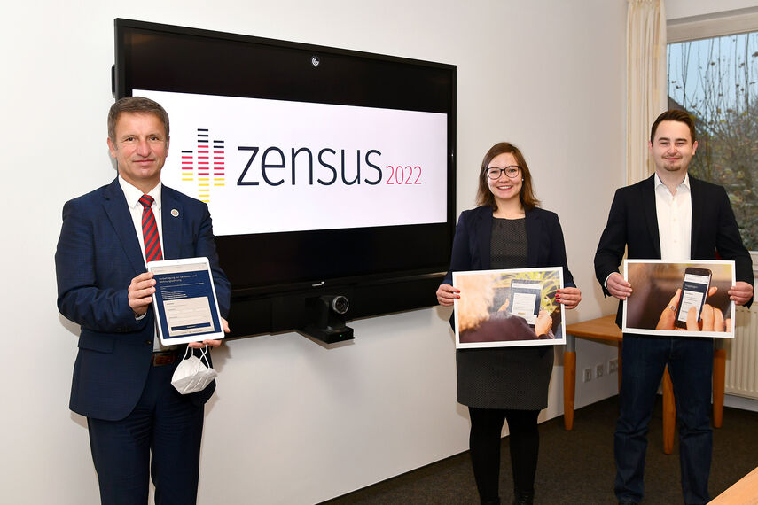 Landrat Michael Stickeln, Alexandra Schodrowski und Robert Stöhr halten Plakate in den Händen. Im Hintergrund ist das Logo 'Zensus 2022' auf einem Bildschirm zu sehen.