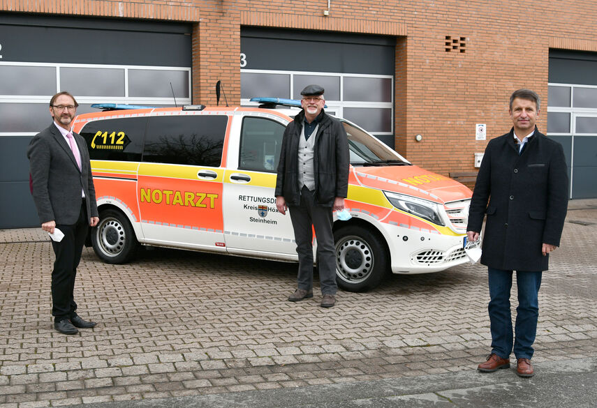 Landrat Michael Stickeln, Dr. Rolf Schulte und Matthias Kämpfer stehen vor einem Notarztwagen.