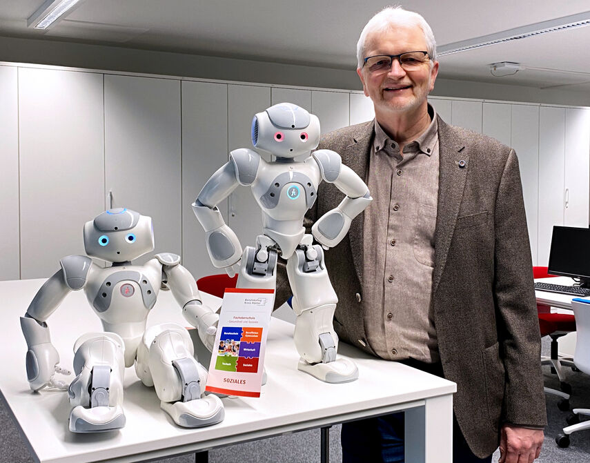 Bildungsgangleiter Dieter Rauchmann zeigt 2 Roboter die auf einem Tisch stehen.