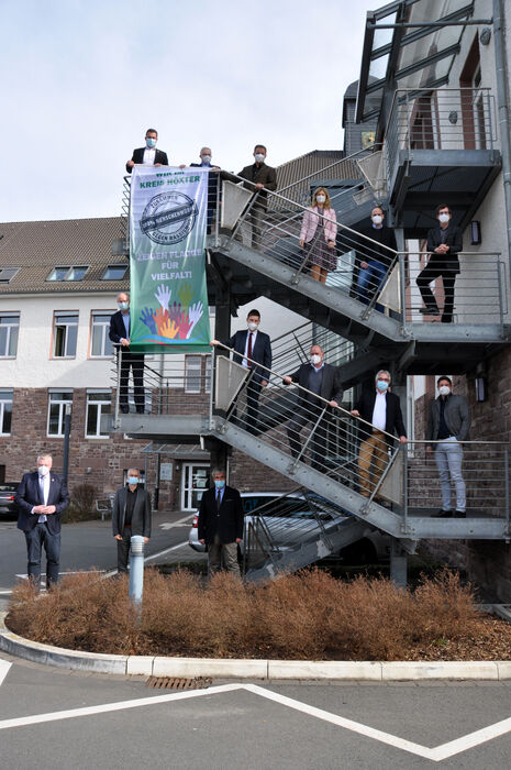 14 Personen stehen auf der Treppe am Kreishaus und zeigen eine große Flagge mit der Aufschrift 'Flagge zeigen für Vielfalt'.
