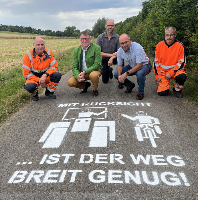 5 Personen knien auf einem Radweg, wo das neue Piktogramm mit der Aufschrift 'Mit Rücksicht ist der Weg breit genug' zu sehen ist.